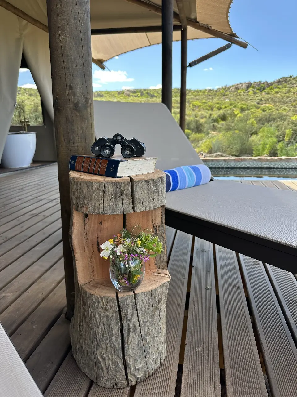 Yamu outdoor deck with wooden stump side table, lounger, and natural landscape backdrop.
