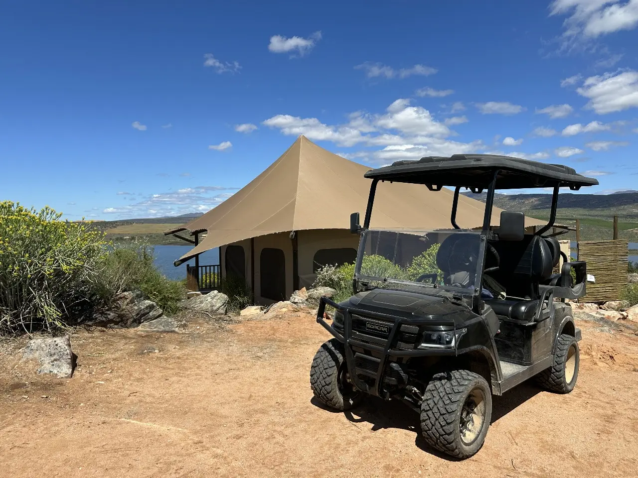 Yamu electric utility cart parked on sandy terrain with canvas tent and mountain views in the background.
