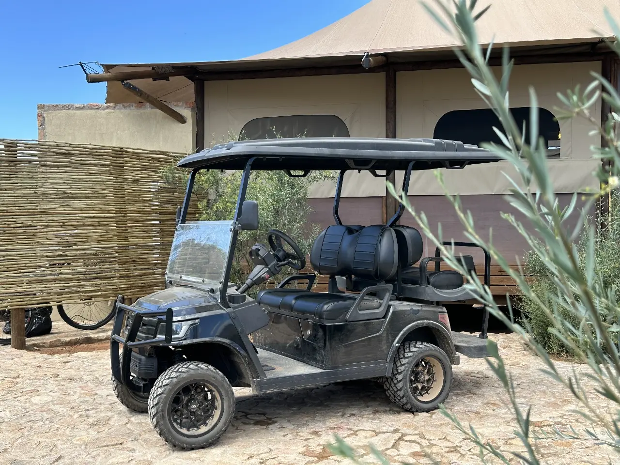 Black utility e-cart parked beside Yamu tent suite with natural stone pathway and reed fencing.