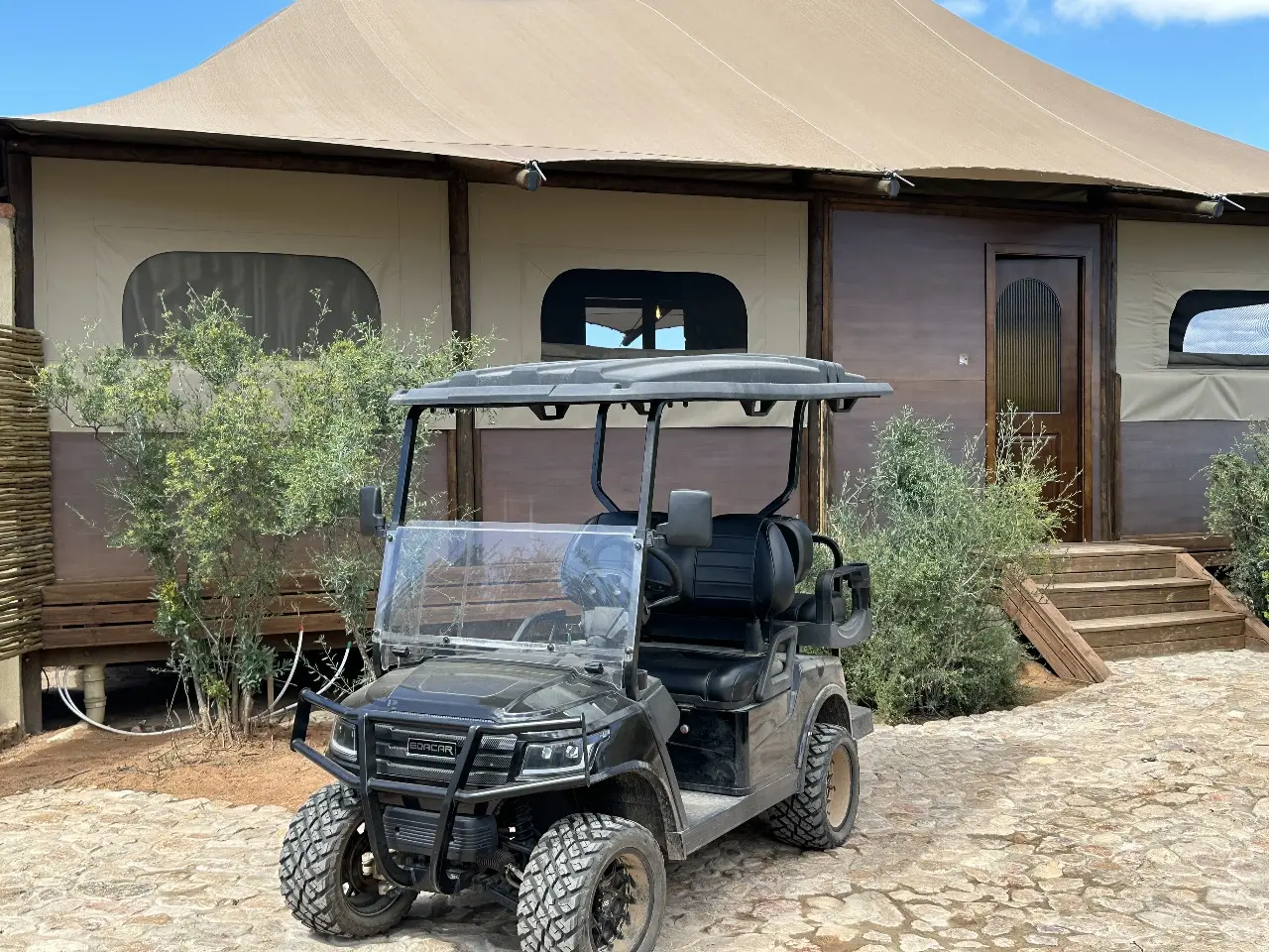 Yamu e-cart positioned at the tent lodge entrance surrounded by native landscaping and wooden structures.