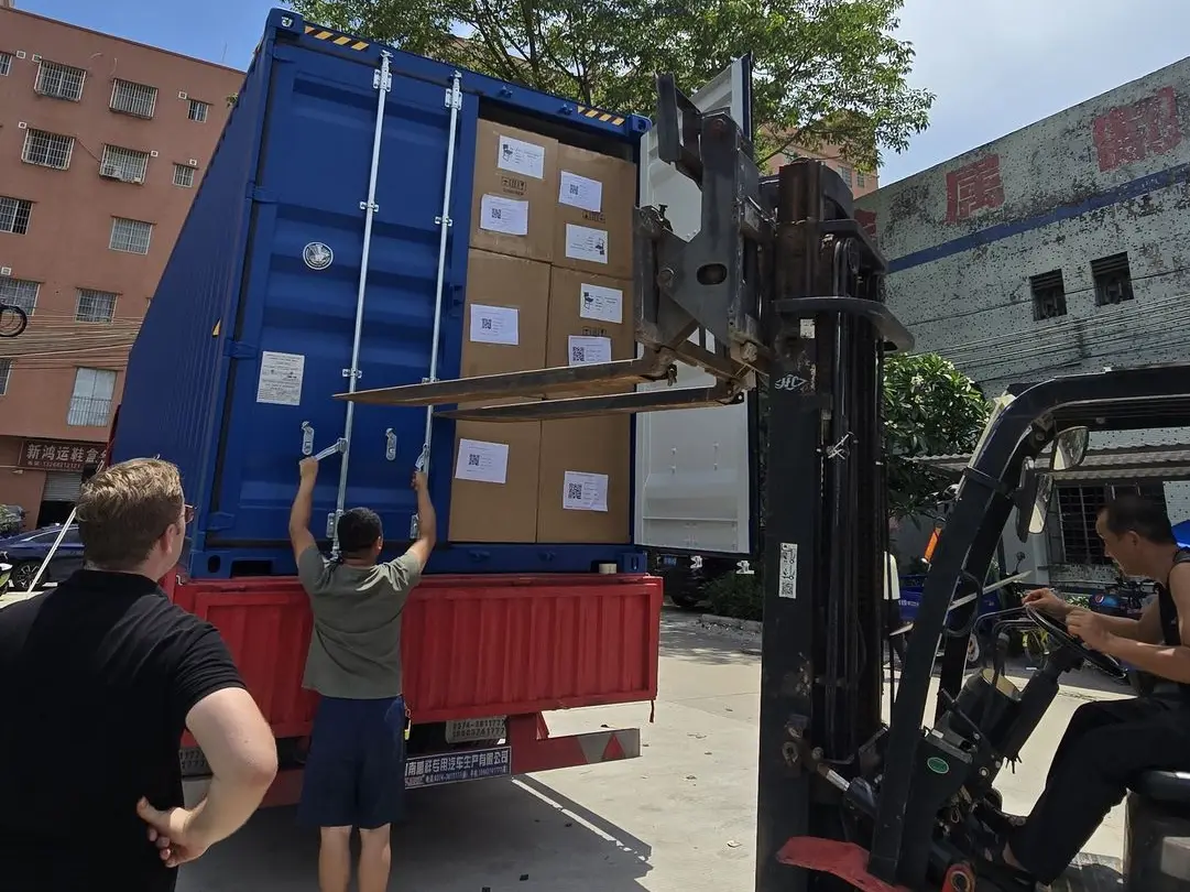 Forklift loading packaged lighting fixtures into a shipping container for delivery overseas.