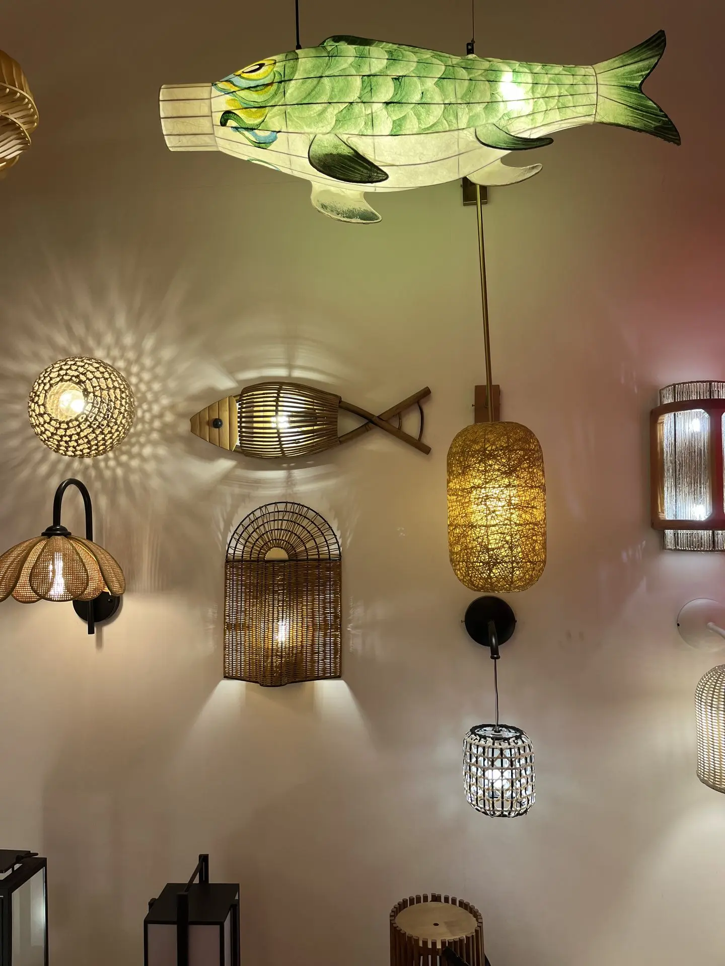 Various rattan light fixtures including wall sconces, pendant lamps, and decorative fish-shaped lighting displayed in a showroom.