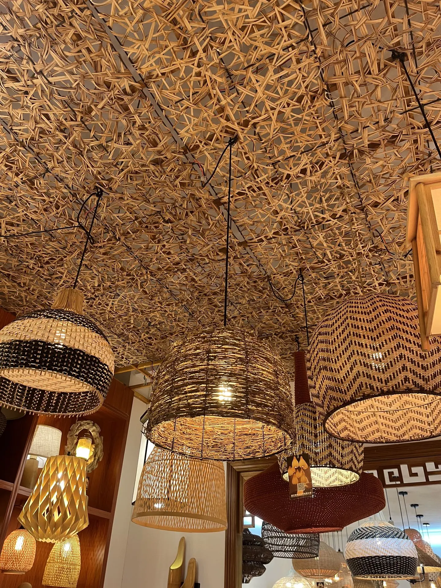Assorted rattan pendant lights displayed in a lighting showroom in China, featuring woven designs in various patterns and shapes.