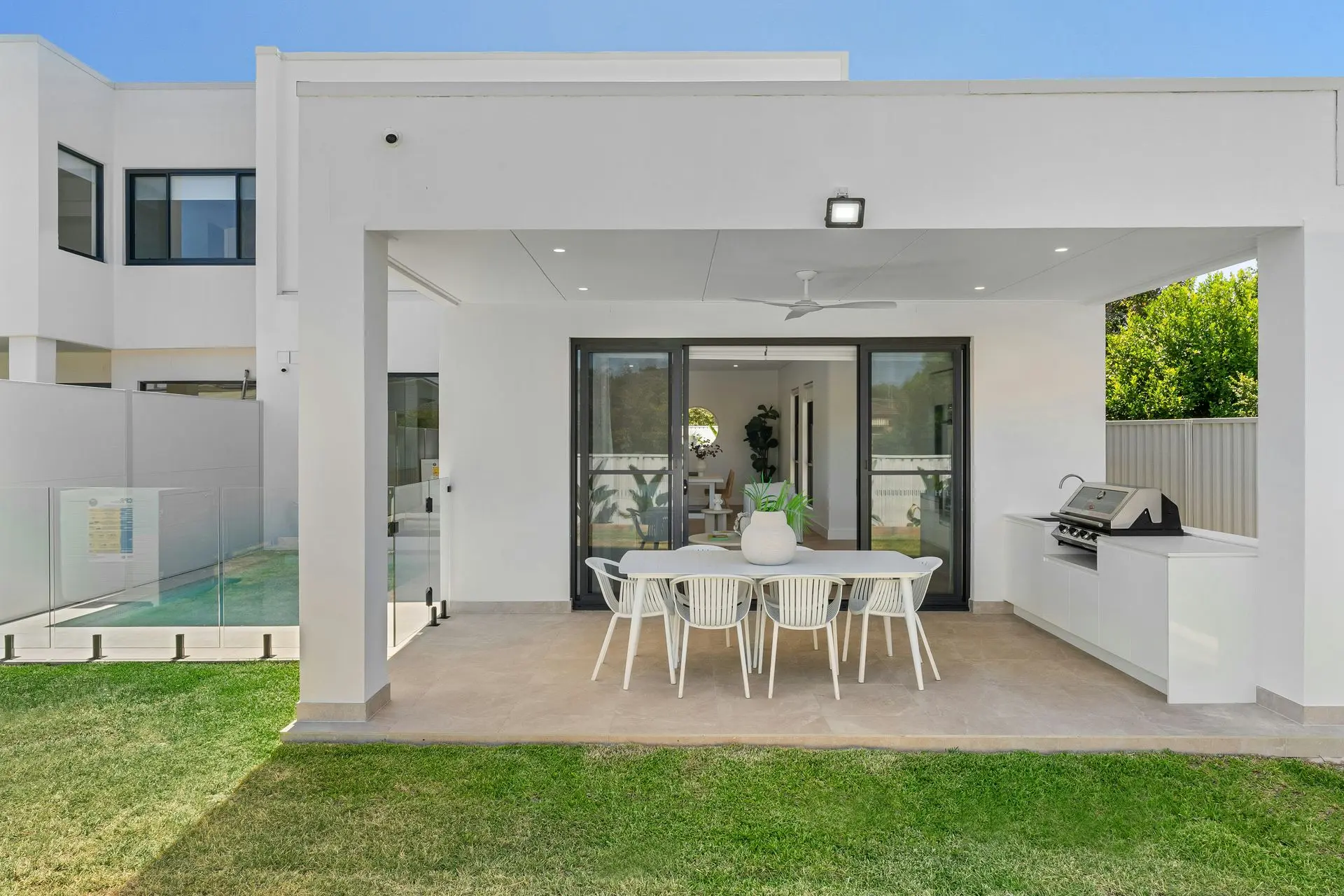 Modern Outdoor Living Area – Custom Patio and Outdoor Kitchen Design Modern outdoor living space with dining setup, sliding doors, and built-in outdoor kitchen under a covered patio.