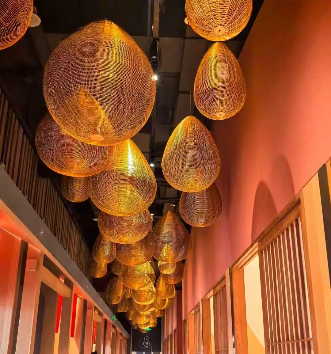 Teardrop-shaped rattan pendant lights installed along a corridor, showcasing custom woven lighting sourced from China