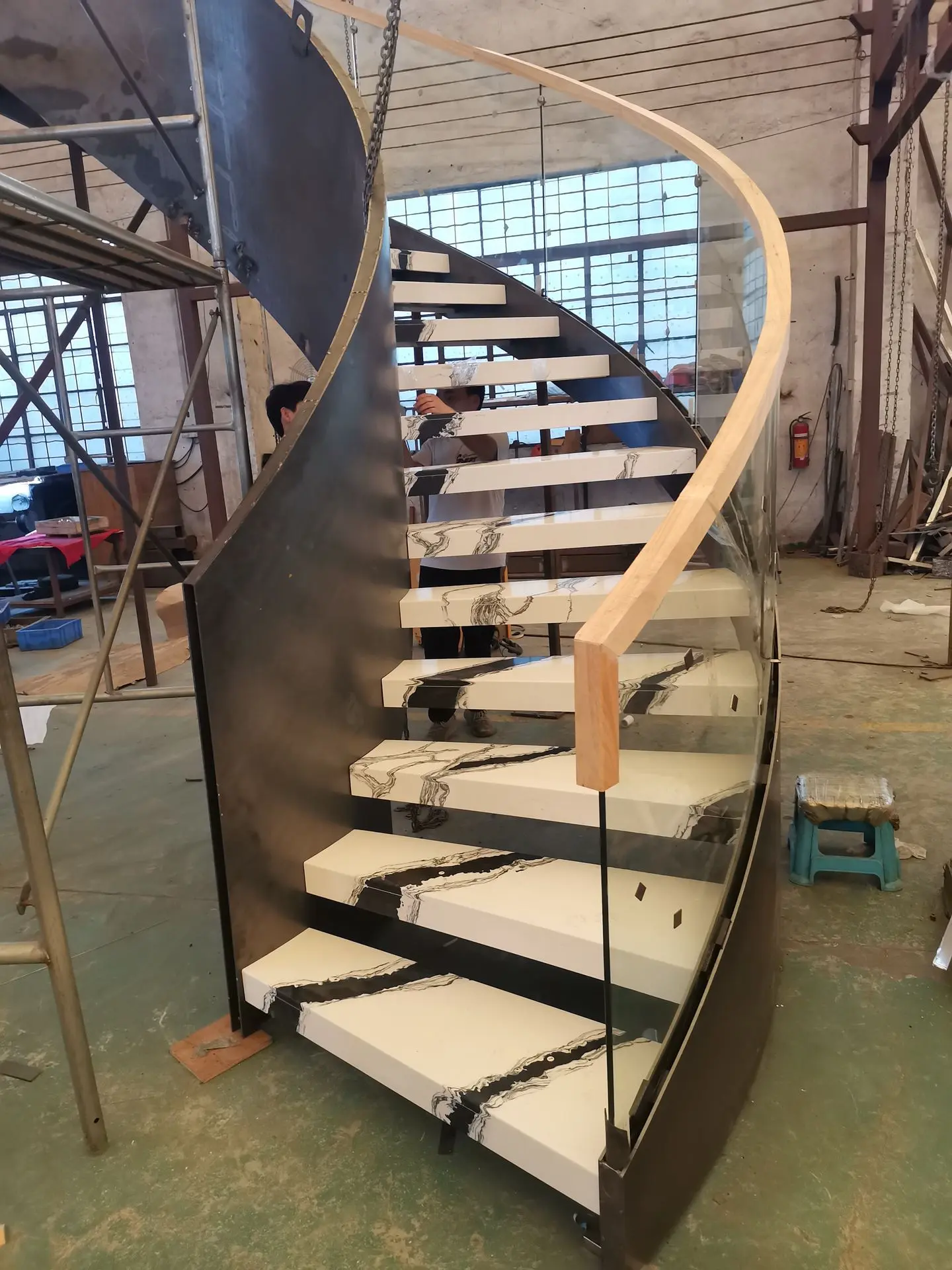 Custom curved staircase manufactured in China with marble-look steps glass balustrade and metal structure