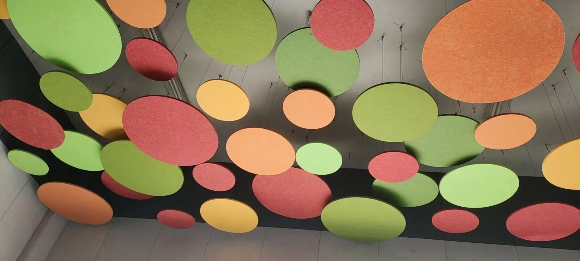 Suspended colorful circular acoustic ceiling clouds in green, orange, and red hanging from a modern ceiling.