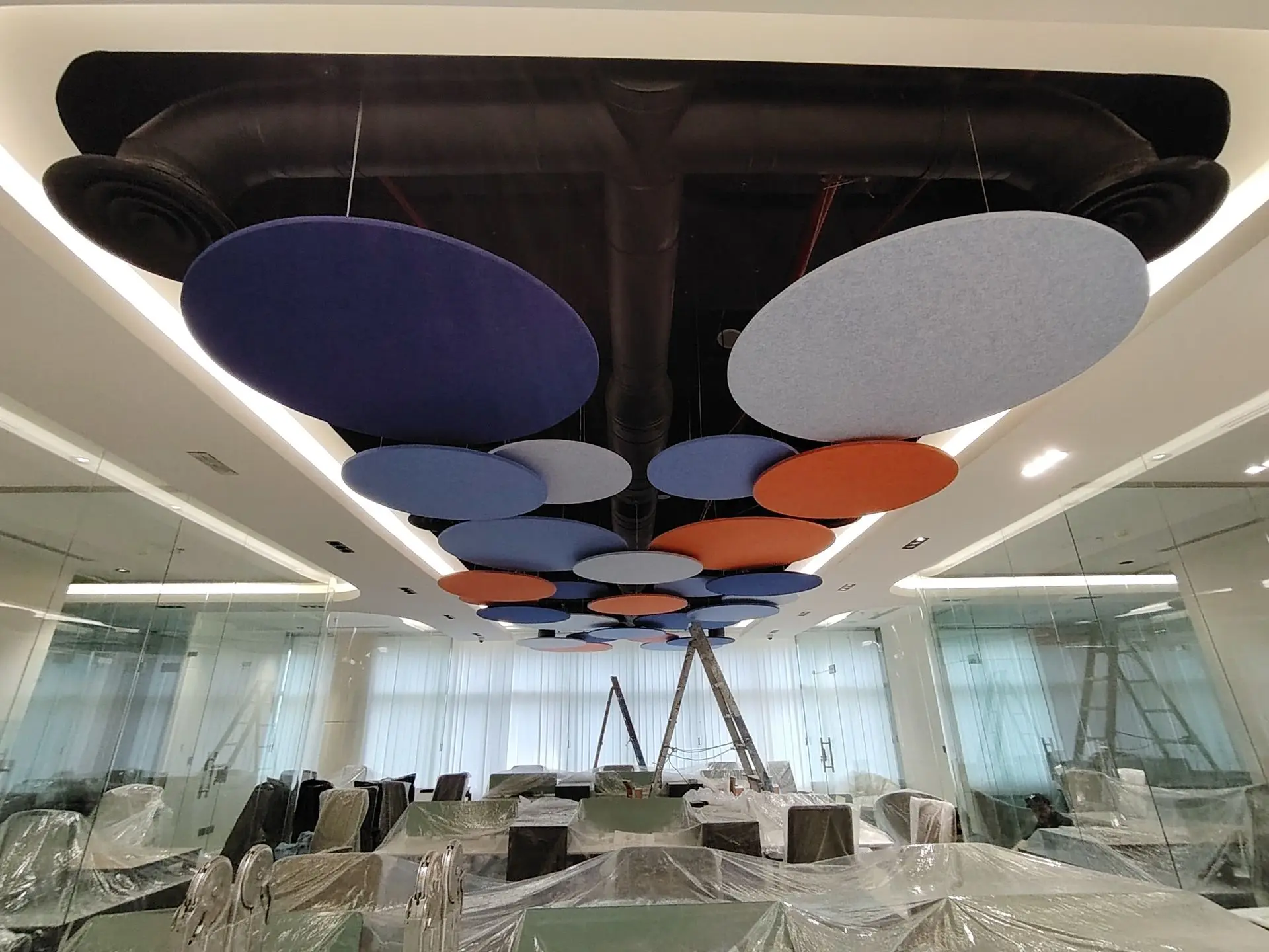 Multi-colored circular acoustic ceiling clouds in vibrant green, orange, and red suspended at different heights for noise reduction.