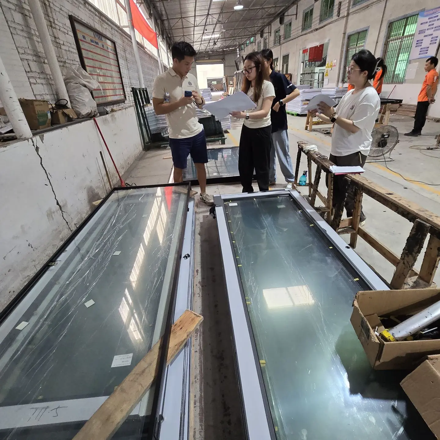 A group of quality control inspectors reviewing window designs and specifications in a manufacturing facility in China, ensuring compliance with standards.