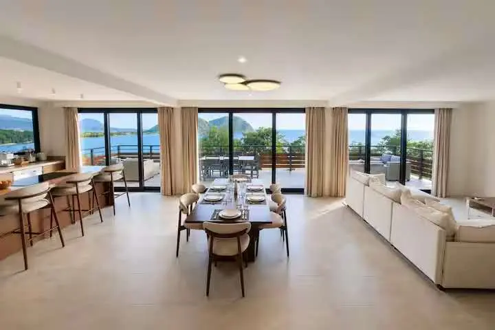 Crystal View open-plan living and dining area with custom furniture, kitchen cabinetry, large windows, and panoramic sea views in Dominica