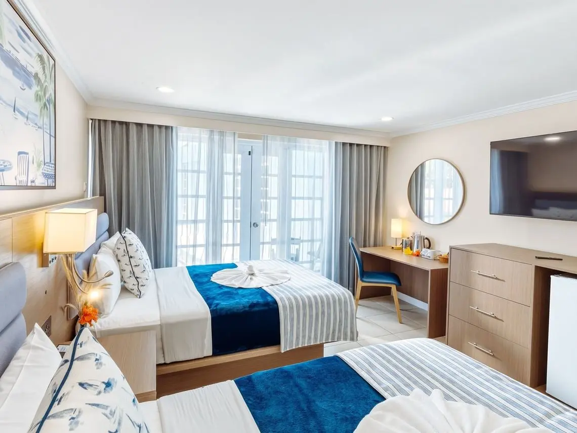 Bay Gardens Marina Haven guest room with twin beds, writing desk, TV console and modern furniture