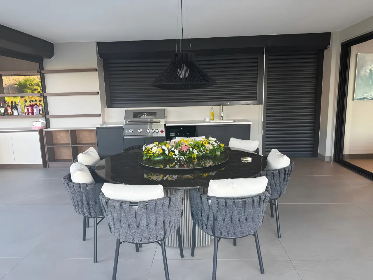 Modern outdoor dining area at a residential villa in Mauritius with round dining table, woven chairs and outdoor kitchen