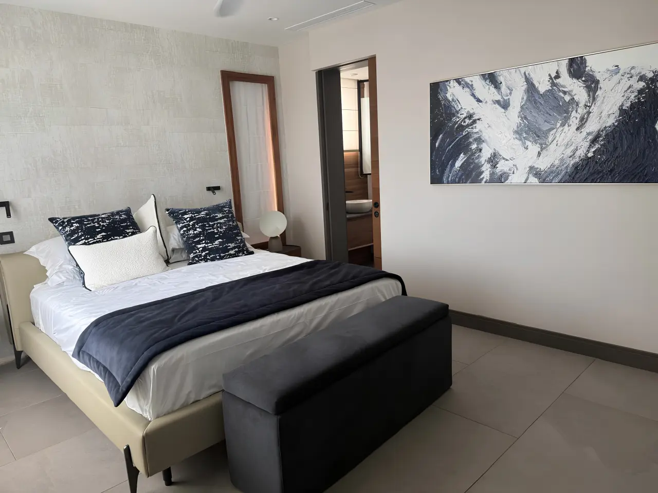 Modern residential villa bedroom in Mauritius with upholstered bed, bench, bedside tables and contemporary artwork